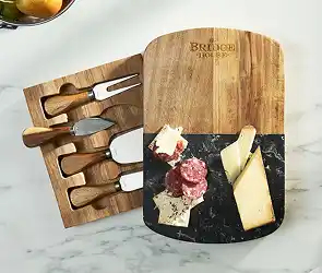 Wooden cheese board with sliced cheeses and salami beside a matching knife set in a storage tray.