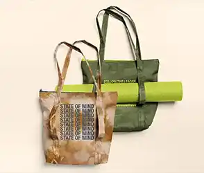 Two reusable tote bags with printed text, one holding a rolled yoga mat.