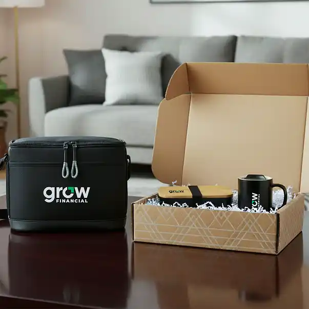Open branded gift box with mug and packaged items next to a black “Grow Financial” cooler bag on a coffee table in a living room.