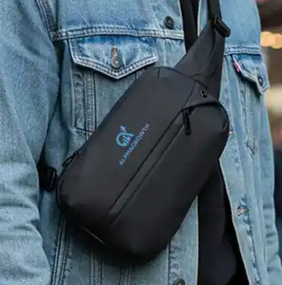 Close-up of a person wearing a black crossbody bag with a small printed logo over a denim jacket.